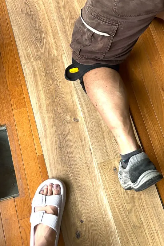 Man's leg and woman’s foot visible while installing waterproof plank flooring over original floors